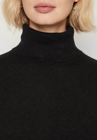 Maglione nero a collo alto con una texture a coste, caratterizzato da un collo alto e dettagli di cucitura discreti al colletto.