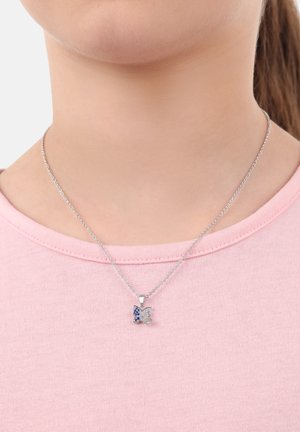 Silberne Kettenhalskette mit einem Schmetterlingsanhänger, der mit blauen und klaren Edelsteinakzenten verziert ist, getragen über einem hellrosa Hemd.