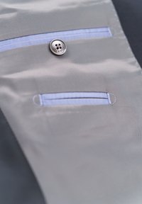 Gray fabric with smooth texture featuring a button and two horizontal pockets with blue accents. Button is silver with floral design.