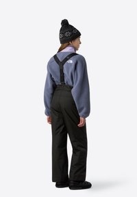 Világoslila polár pulóver, fekete vízálló nadrág nadrágtartóval, fekete mintás sapka és fekete slip-on cipő.