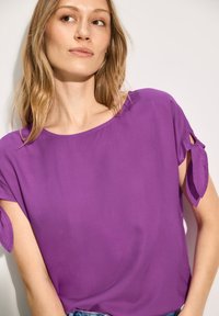 Maglietta a maniche corte in vivace tessuto viola, con dettagli annodati alle maniche e una vestibilità comoda, dal texture morbida.