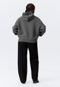 Sweat à capuche gris, coupe décontractée, avec ourlet et poignets côtelés, associé à un pantalon noir taille haute à jambes larges et des bottines.