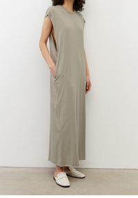 Sukienka maxi w jasnoszarym materiale, z krótkimi rękawami, bocznymi rozcięciami i przednimi kieszeniami, w połączeniu z białymi butami wsuwanymi. Gładka tekstura, luźny krój.