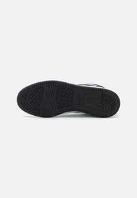 Black rubber sneaker sole featuring textured grip patterns, a circular logo, and a wide base for stability. Smooth edges and reinforced heel section.
