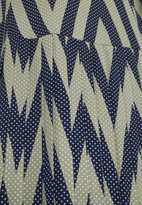 Tessuto intrecciato con un motivo a zigzag in blu navy e verde khaki, con pois bianchi, che presenta un design testurizzato e stratificato.