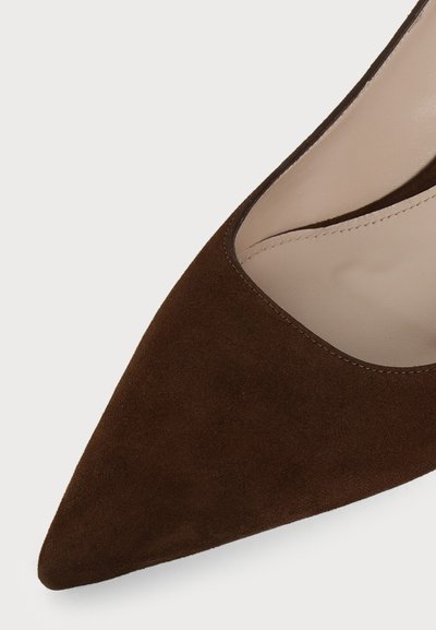 Gros plan sur le bout pointu d’une chaussure femme en daim marron avec une doublure intérieure beige et des coutures visibles.