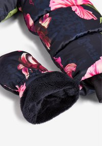 Sección de chaqueta acolchada floral con tejido azul oscuro, con vibrantes flores rosas y blancas, puños elásticos forrados con suave forro de lana negra.