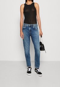 Black sleeveless top, blue denim jeans with a straight fit, black and white sneakers, and a small black handbag.
