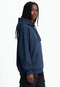 Sweat à capuche bleu marine en tissu de coton doux, avec une poche frontale, une capuche à cordon ajustable, des poignets et un ourlet côtelés.