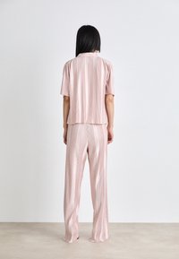 Gestreiftes, rosa Koordinatenset aus Strick, das ein kurzärmeliges Oberteil und weite Hosen umfasst, beide mit vertikalen Streifen und einem lässigen Schnitt.