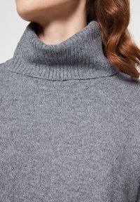 Grauer Rollkragenpullover mit geripptem Muster, entspanntem Schnitt und weichem Strickmaterial, mit betonten Kragen- und Schulterdetails.