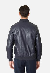 Giacca bomber in pelle blu navy con colletto e polsini a coste, caratterizzata da una finitura liscia e una forma leggermente aderente. La vista posteriore evidenzia i dettagli delle cuciture.
