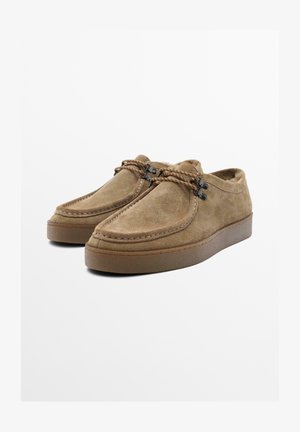 Brązowe wsuwane buty z zamszu z zaokrąglonym noskiem, kontrastującym przeszyciem i plecionymi sznurowadłami. Miękka wyściółka wewnętrzna i płaska gumowa podeszwa.