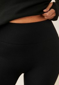 Černé žebrované legíny s vysokým pasem, vyrobené z elastického materiálu. Viditelný texturovaný vzor a bezšvový design v pase a na bocích.