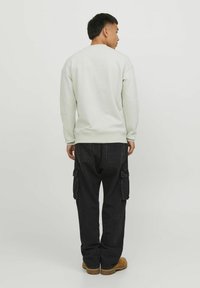 Sudadera gris claro con cuello redondo y puños acanalados, combinada con pantalones cargo negros que cuentan con bolsillos laterales y un corte relajado.