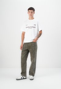 White t-shirt with "Functional Aesthetics" text in dark purple, paired with olive green textured pants and black-accented white sneakers.