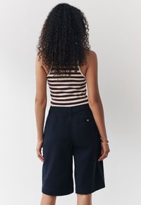 Haut débardeur rayé et ajusté avec un col dégagé, associé à un short bleu marine longueur genou, doté d'une poche arrière et d'un bouton doré.