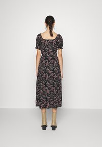 Vestido preto de flores com mangas curtas bufantes, corpete ajustado e saia fluida, combinado com botas de tornozelo bege e um penteado trançado.