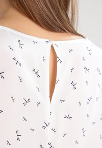 Hvid bluse med navy blå guldsmedemønster, der har lukning med nøglehul bagpå og blødt, let stof.