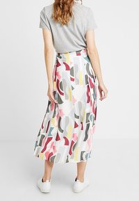 Falda midi plisada en un tejido liviano, con un estampado abstracto colorido que presenta formas en rosa, gris y amarillo. Detalle de abertura lateral visible.