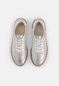 Stříbrné tenisky s texturovaným metalickým povrchem, bílými tkaničkami a světle hnědou gumovou podrážkou. Zaoblený tvar se sportovními designovými prvky.