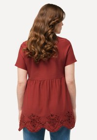 Top rojo de manga corta con cintura fruncida y dobladillo con forma de concha, adornado con bordado floral, combinado con vaqueros azules.