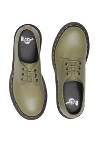 Scarpe in pelle verde oliva con suole in gomma nere, punta rotonda e cinque occhielli per i lacci. Presentano cuciture gialle attorno alla suola.