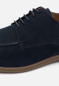 Pantofi din suede albastru închis, cu șireturi tonale, o talpă netedă și detalii cusute pe laturi pentru un plus de textură și interes de design.