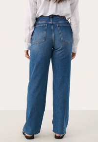 Jeans de tiro alto y pierna ancha en denim azul medio, con dos bolsillos traseros y dobladillos deshilachados, mostrados desde la vista trasera.