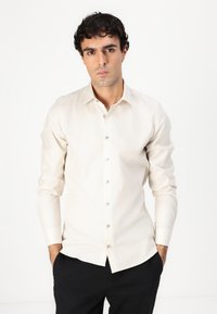 Beige langermet skjorte med knapper i en glatt teksturert stoff, med klassisk krage og perlemorsknapper.