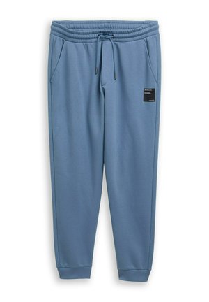 Niebieskie spodnie dresowe wykonane z miękkiego materiału, wyposażone w elastyczny pas, sznurek do regulacji, boczne kieszenie oraz naszywkę z logo na lewej nogawce.