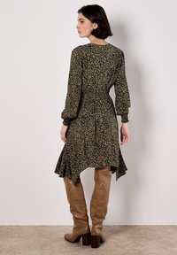 Leopardenmusterkleid mit geraffter Taille, langen Ärmeln und asymmetrischem Saum. Kombiniert mit tanfarbenen kniehohen Stiefeln mit Absatz. Texturierter Stoff.