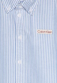 Csíkos, világoskék és fehér ing. Pamut anyag, amely puha tapintású. A mellkasán egy kis piros "Calvin Klein" címke található.