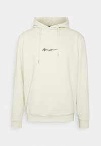 Hoodie color crema realizzato in morbido tessuto, con tasca frontale, cordini e un logo ricamato nero sul petto.