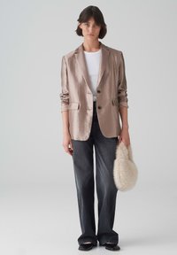 Hellbeige Satin-Blazer mit zwei Knöpfen, zwei Fronttaschen und hochgeschlagenen Ärmeln, kombiniert mit dunklen, weit geschnittenen Jeans und einer flauschigen Creme-Handtasche.