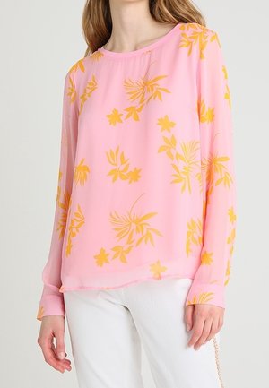 Blouse rose à manches longues, avec un motif floral jaune. Tissu léger et transparent, col rond et coupe décontractée.