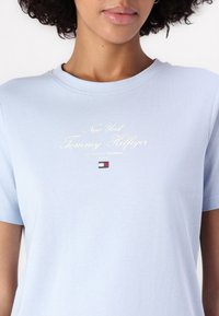 Ljusblå bomullströja med kort ärm, med vit skrivtext och en liten logotyp i mitten. Slät textur, rund halsringning.