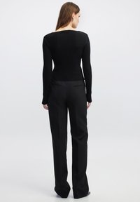 Schwarzer gerippter Pullover mit langen Ärmeln, kombiniert mit schmal geschnittenen schwarzen Hosen. Beide Kleidungsstücke haben eine glatte Textur und ein minimalistisches Design.