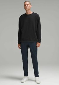 Črna majica s kapuco z okroglo ovratnico, dolgimi rokavi in sprednjim žepom, v kombinaciji z navy slim-fit hlačami in belimi športnimi copati.