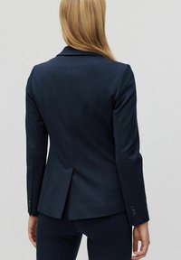 Marinblå blazer i slätt tyg, med notchad krage, två bakslitsar och knäppte ärmslut, skräddarsydd för en figurnära look.