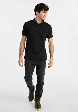 Czarny polo z krótkim rękawem i trzema guzikami, w zestawieniu z ciemnoszarymi dżinsami i zielonymi butami. Prosty i klasyczny design.