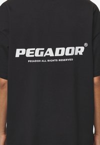 Black t-shirt with large white "PEGADOR" text and smaller "PEGADOR ALL RIGHTS RESERVED" printed below on the front center.