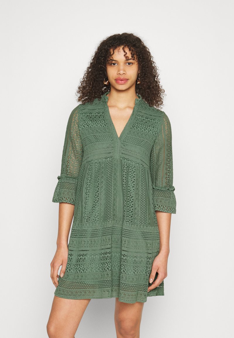 Green lace dress featuring a v-neckline, three-quarter sleeves, textured patterns, and a loose, flowing design.