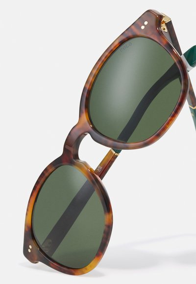 Skilpadde-skjold solbriller med grønne linser, preget av en dristig, avrundet form og metallakenter nær hengslene.