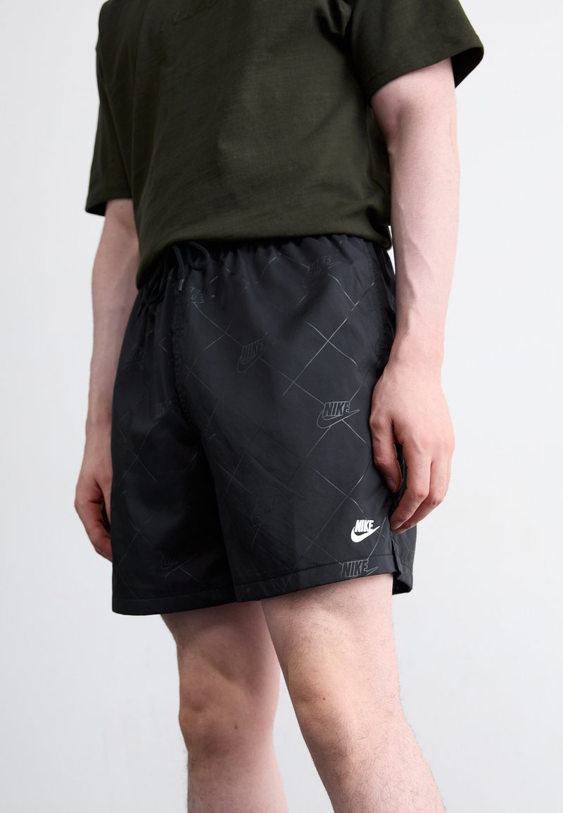 Schwarze Nike-Shorts mit einem rautenförmigen Muster, ausgestattet mit einem elastischen Bund und Kordelzug. Weißes Nike-Logo am Saum und an der Seite. Glatte Stoffoberfläche.