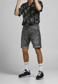 Black short-sleeve shirt with green palm leaf print, paired with gray distressed denim shorts and black sneakers with white accents.