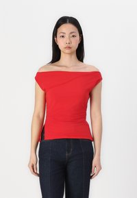 Red off-the-shoulder top made of smooth fabric with side ruching and a fitted design, paired with dark denim jeans.