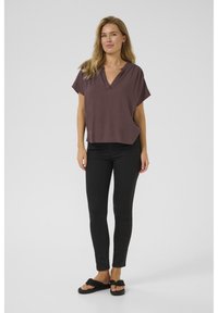 Top mauve à manches courtes avec un décolleté en V, associé à un jean noir slim-fit et des sandales noires, présentant un matériau texturé et une coupe décontractée.