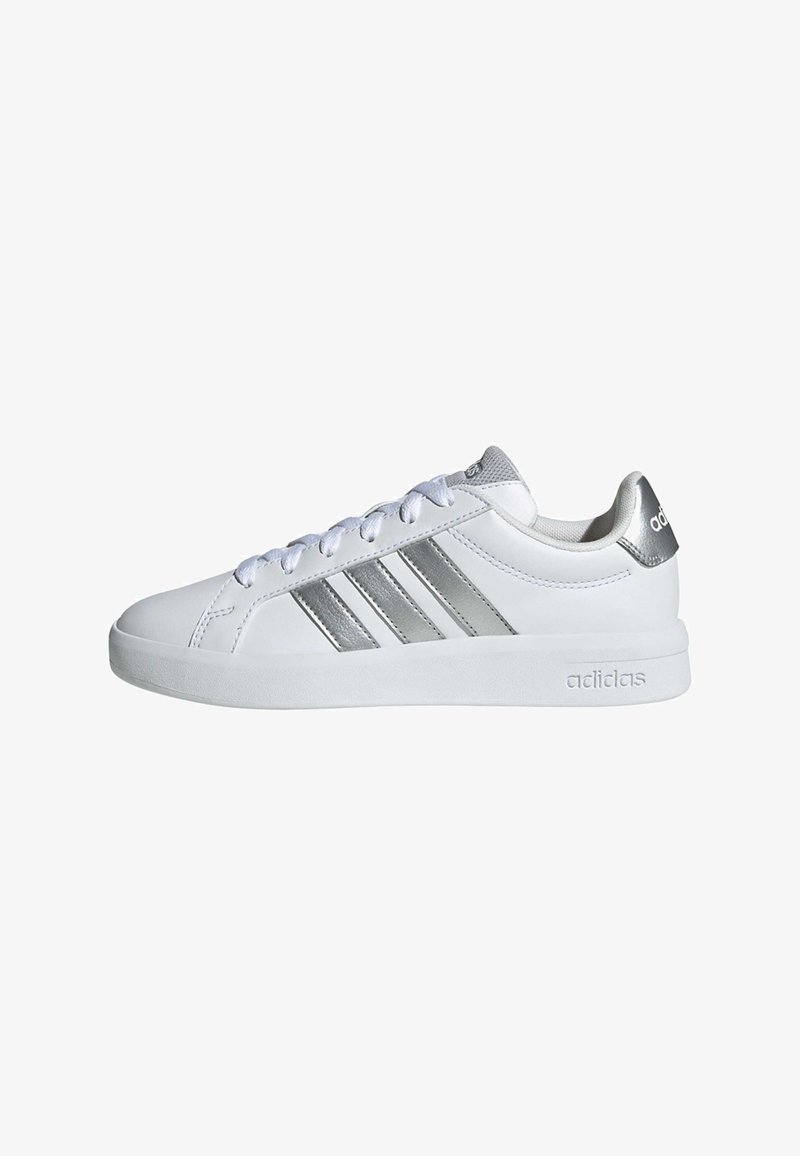 Weißer Adidas-Sneaker mit silbernen Streifen, weißen Schnürsenkeln und silbernem Fersenriemen, von der Außenseite vor weißem Hintergrund gesehen.