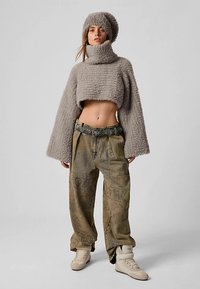 Pull court texturé gris avec manches larges, associé à un pantalon kaki taille haute, ample, avec un motif et une ceinture.